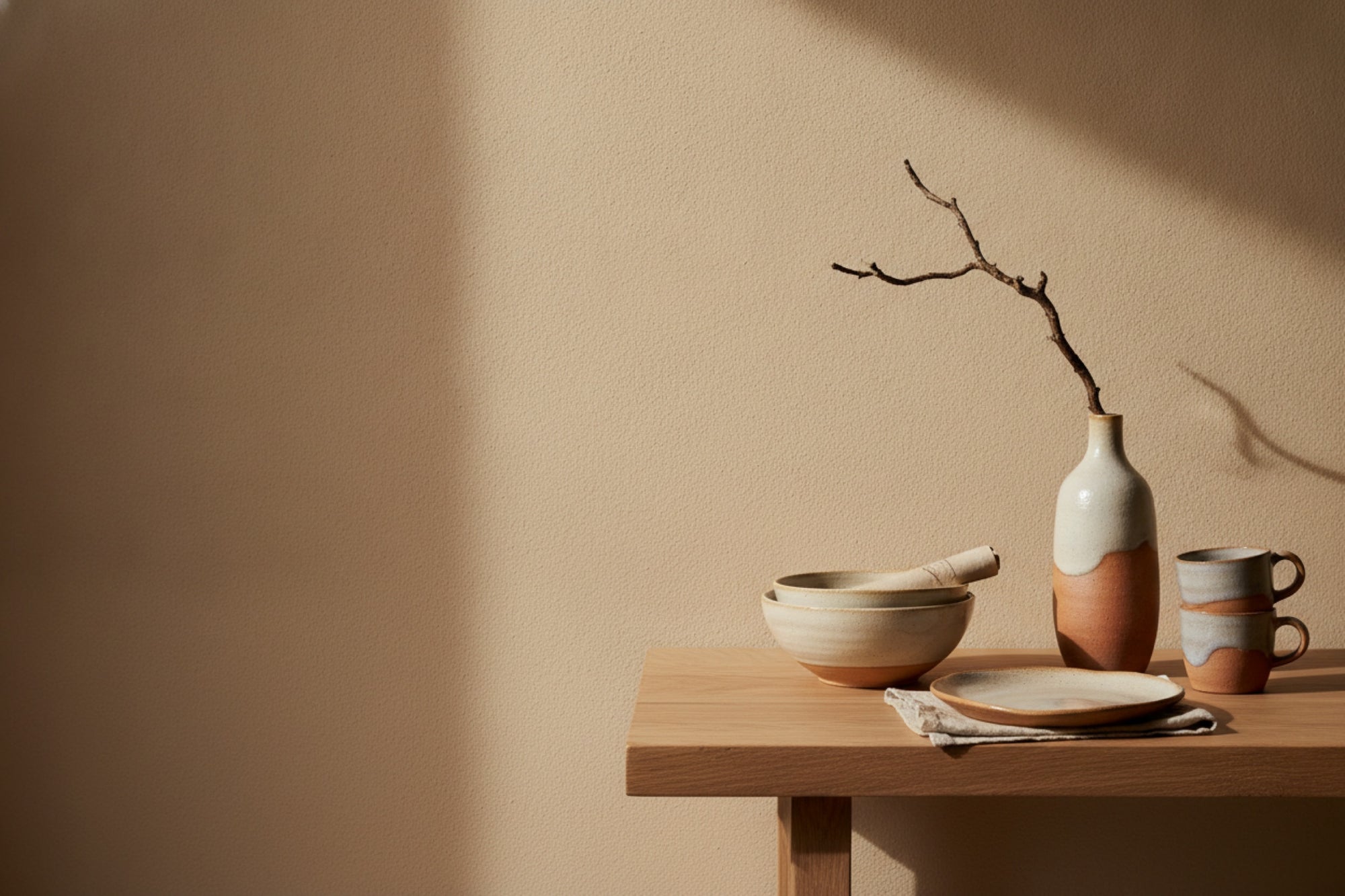 Stoneware bowls, mugs and a vase on an oak table in warm daylight